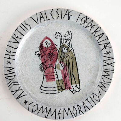 Assiette commémorative des 150 ans de l’entrée du Valais dans la Confédération, représentant saint Théodule, avec un cep de vigne et la cloche, 1965© Musées cantonaux du Valais - Robert Hofer, Musée d’histoire du Valais