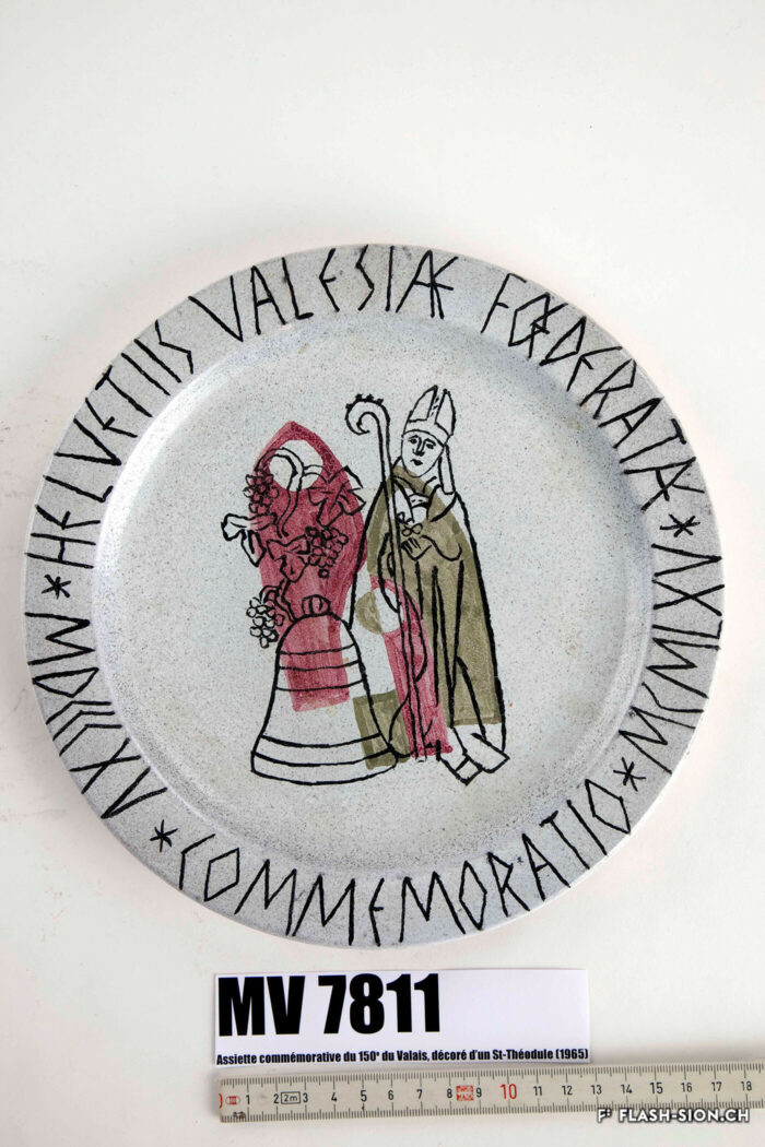 Assiette commémorative des 150 ans de l’entrée du Valais dans la Confédération, représentant saint Théodule, avec un cep de vigne et la cloche, 1965© Musées cantonaux du Valais - Robert Hofer, Musée d’histoire du Valais