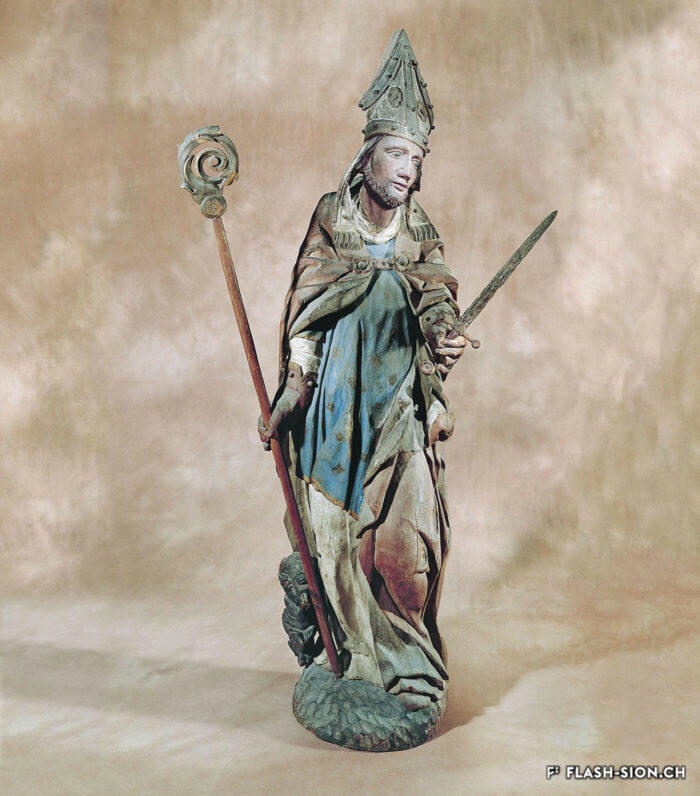 Sculpture représentant saint Théodule, tenant la crosse et le glaive, et accompagné du diablotin portant une cloche. Mélèze polychromé, 16e siècle © Musées cantonaux du Valais - Jean-Yves Glassey, Musée d’histoire du Valais
