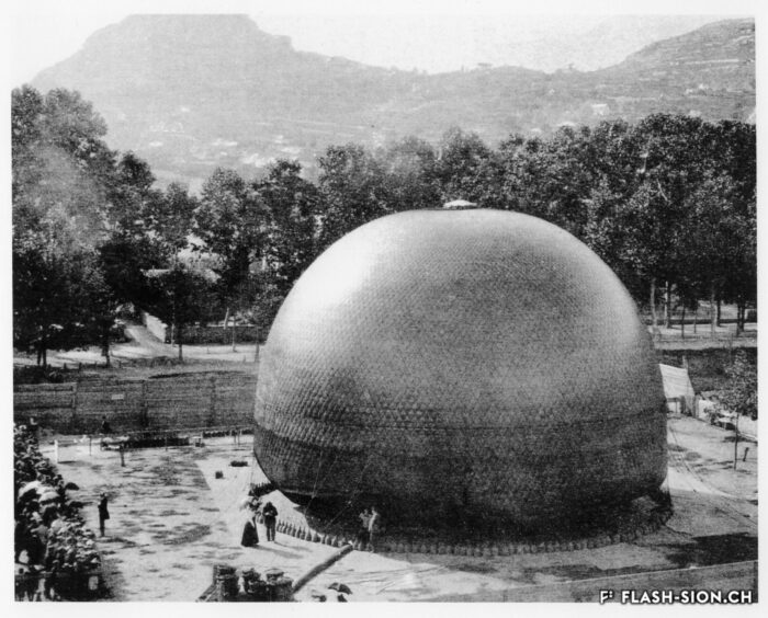 Le « WEGA » lors du gonflement. En bas à gauche, on discerne le générateur d’hydrogène, à gauche le Prof. Forel donne des explications au public présent, 29 septembre 1898 © Forstadjunkt Schönenberger, reproduction Archives de la Ville de Sion