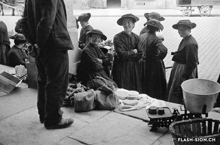 Paysannes sur les marches de la grenette, vendant fromages et autres marchandises lors du marché, vers 1933 © Raymond Schmid, Bourgeoisie de Sion, Médiathèque Valais – Martigny