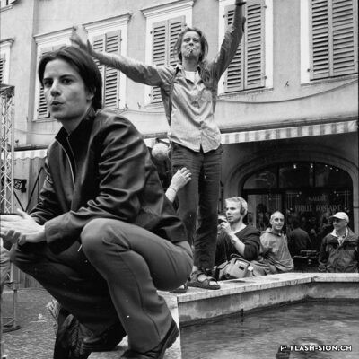 Marianne Bruchez, le « visage » de la Pride de 2001, sur la fontaine du Grand-Pont (Lionel Baier, réalisateur, en arrière-plan) © Bernard Dubuis, Enquête photographique en Valais, Médiathèque Valais – Martigny